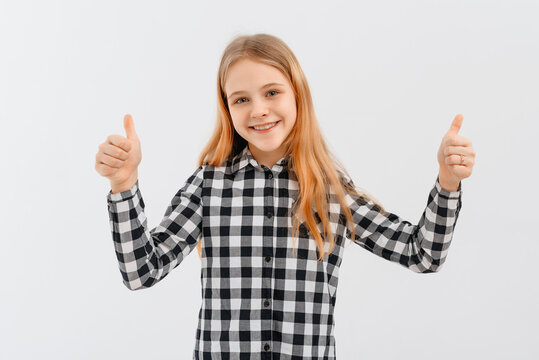 Portrait of young girl happy positive smile showing thumbs-up, standing over white background in casual shirt