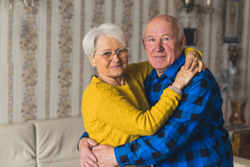 Loving old senior family couple in love smiling and hugging in the living room at home, enjoying...