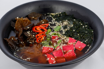 Korean dish soup with mushroom noodles and tofu cheese in a black plate
