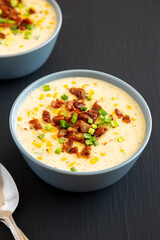 Homemade Corn Chowder with Bacon in a Bowl on a black background, side view.