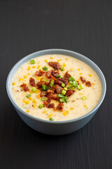 Homemade Corn Chowder with Bacon in a Bowl on a black background, side view.