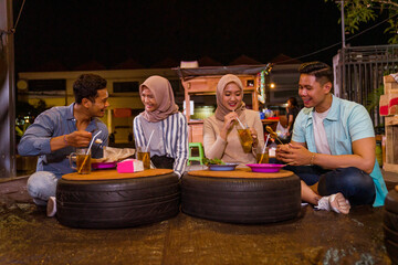 portrait of happy muslim friend enjoy having iftar dinner at traditional food stall sitting on the floor