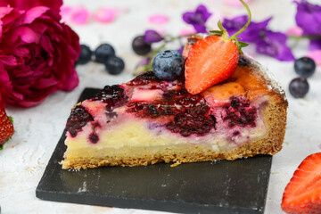 berry cheesecake decorated with strawberries on a black slate on a light background
