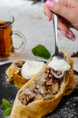 dessert apple roll with ice cream on black slate on table with spoon in female hands
