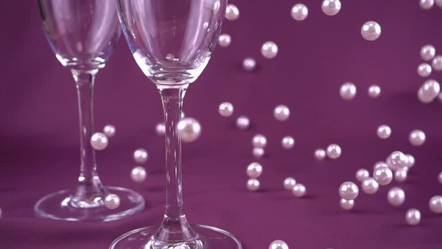 Falling white pearls next to wine glasses on a purple