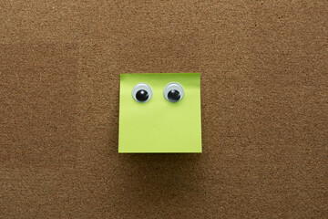 googly eyes on clean green  sticky note on cork board concept using sticky notes 