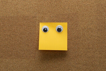 googly eyes on clean orange  sticky note on cork board concept using sticky notes 