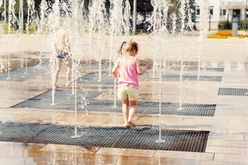 child girl playing in the water jets of the fountain