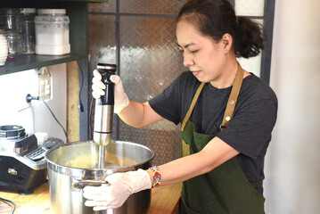 Young Vietnamese woman stirring  dough in a big metal saucepan