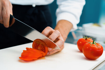 Close-up of a chef slicing tomato in a professional restaurant kitchen
