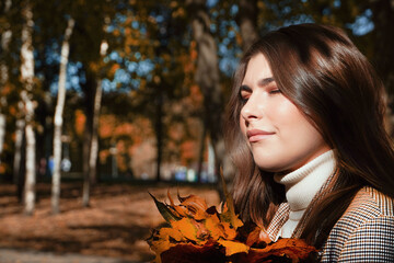  Smilng dreaming young woman at autumn park. Woman holding in her hands fallen autumn leaves.