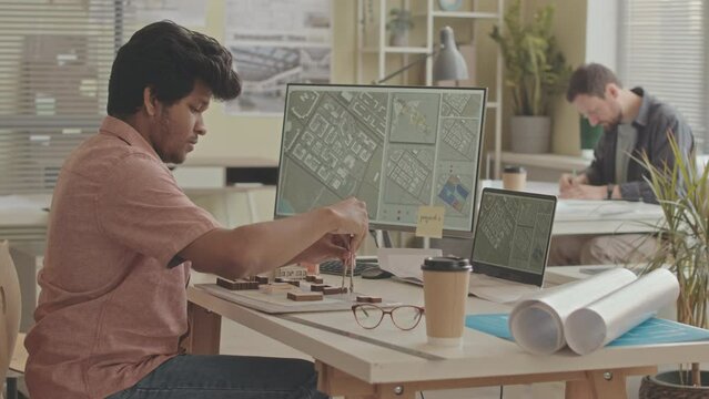 Waist up slowmo of Biracial male city planner looking at city map while designing city plan in office, working there with colleague