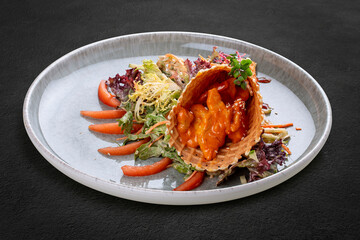 Salad with sweet and sour chicken in a waffle cone on a bed of lettuce leaves. On a dark background, isolated.