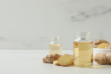 Glass bottle of essential oil and ginger root on white table, space for text