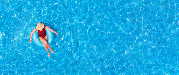 Zenith aerial view of a swimming pool in summer. Young girl in a swimsuit and hat floating with...