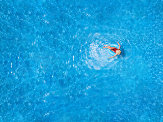 Zenith aerial view of a swimming pool in summer. Young girl in a swimsuit and hat floating with blue donut.
