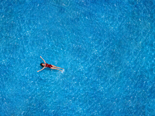 Obraz premium Aerial view of a swimming pool in summer. Young woman in a swimsuit swimming and refreshing.