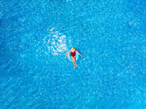 Zenith aerial view of a swimming pool in summer. Young girl in a swimsuit and hat floating with blue donut.