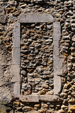 Weathered old stone frame of a bricked up window in a rough stone wall facade of a typical house in Vallon-Pont-d'Arc, Provence, southern France. Background illuminated by bright summer sunlight.