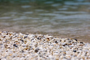 Small pebble stones on sea beach with transparent water. Natural background for summer vacation