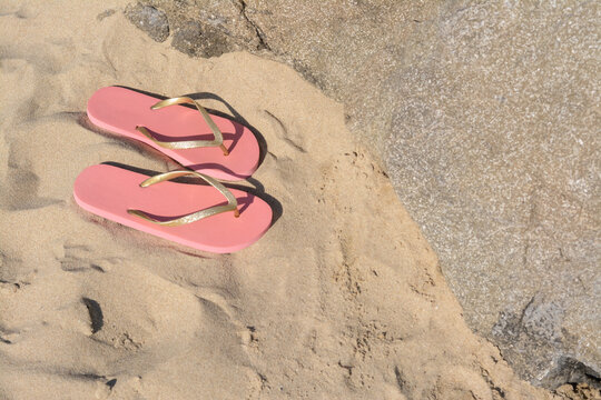 Stylish pink flip flops on sandy beach near rock