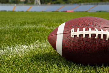 American football ball on green field grass in stadium, closeup