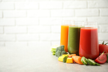 Different tasty juices and fresh ingredients on grey table against brick wall. Space for text