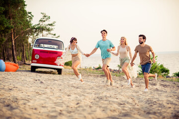 Photo of positive cheerful buddies company holding hands riding retro bus outdoors countryside forest