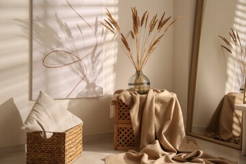Vase with decorative dried plants and painting in stylish room interior