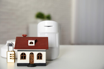 House model, lock, smoke and movement detectors on table in room, space for text. Home security...