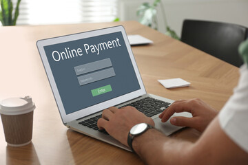 Man using laptop for online payment at wooden table, closeup