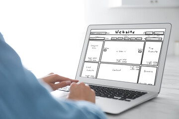 Designer creating website on laptop at white table, closeup