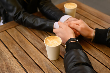 Lovely couple with coffee holding hands together at wooden table outdoors, closeup. Romantic date