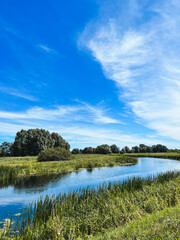 Summer rural river landscape on a sunny day. Countryside panorama with grass, trees and sky in Europe.