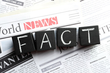 Obraz premium Word FACT made with black cubes on pile of newspapers, flat lay