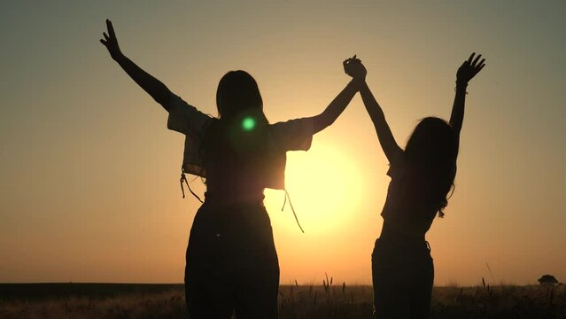 silhouette of a happy two girls and happy time sunset. Holding hands up