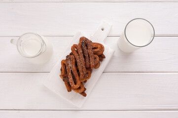 Homemade churros with milk and cream on a white wooden background.