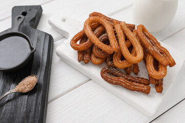 Homemade churros with chocolate on a white wooden background.