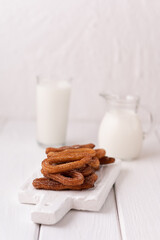 Homemade churros with milk and cream on a white wooden background.