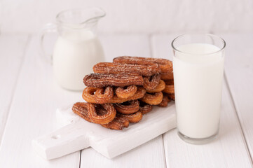 Homemade churros with milk and cream on a white wooden background.