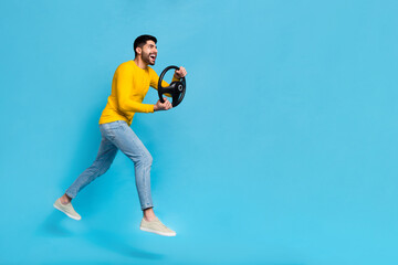 Full body profile photo of excited carefree handsome guy hands hold wheel jump run empty space isolated on blue color background