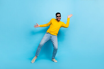 Full length photo of funky pretty man wear yellow sweater dark glasses dancing isolated blue color...