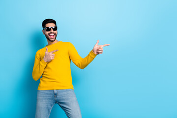 Naklejka premium Photo of pretty excited man wear yellow sweater dark glasses dancing pointing empty space isolated blue color background