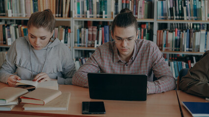 group of concentrated students preparing for examination while sitting at table in university library indoors