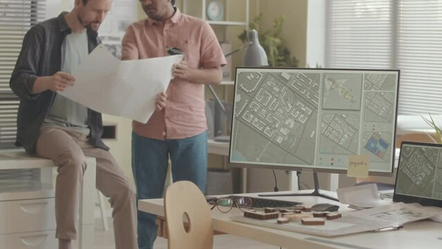 Cropped slowmo of two professional architects holding rolled out sheet of paper in hands discussing drawing plan of building