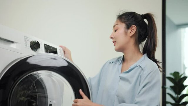Happy beautiful housewife opening the front of the washing machine using washing machine to clean dirty clothes at house. Woman cleaning clothes on weekends..