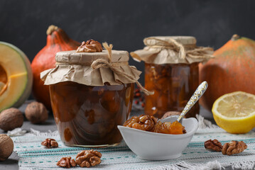 Homemade pumpkin jam with lemon and walnuts in jars and bowl on dark gray background