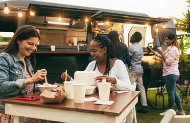 Happy multiracial senior women eating at food truck restaurant outdoor - Focus on african female face