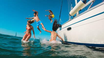 Happy friends diving from sailing boat into the sea - Main focus on sailboat