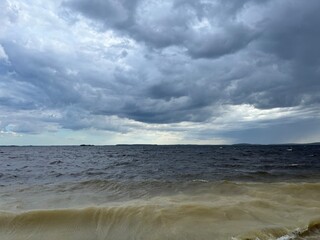 Sandy coastline of the forest lake, cloudy sky, dramatic landscape